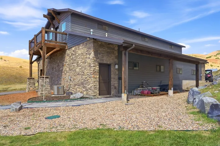 Stone and siding exterior with a wood-frame balcony and covered patio area