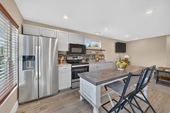 Stainless steel appliances, light-toned cabinetry, wood-finish flooring, recessed lighting, and a tiled backsplash