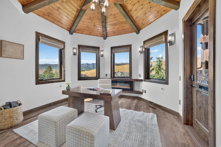 Vaulted wood-paneled ceiling with exposed beams, multiple windows, wood-finish flooring, built-in electric fireplace, and a wood-paneled entry door
