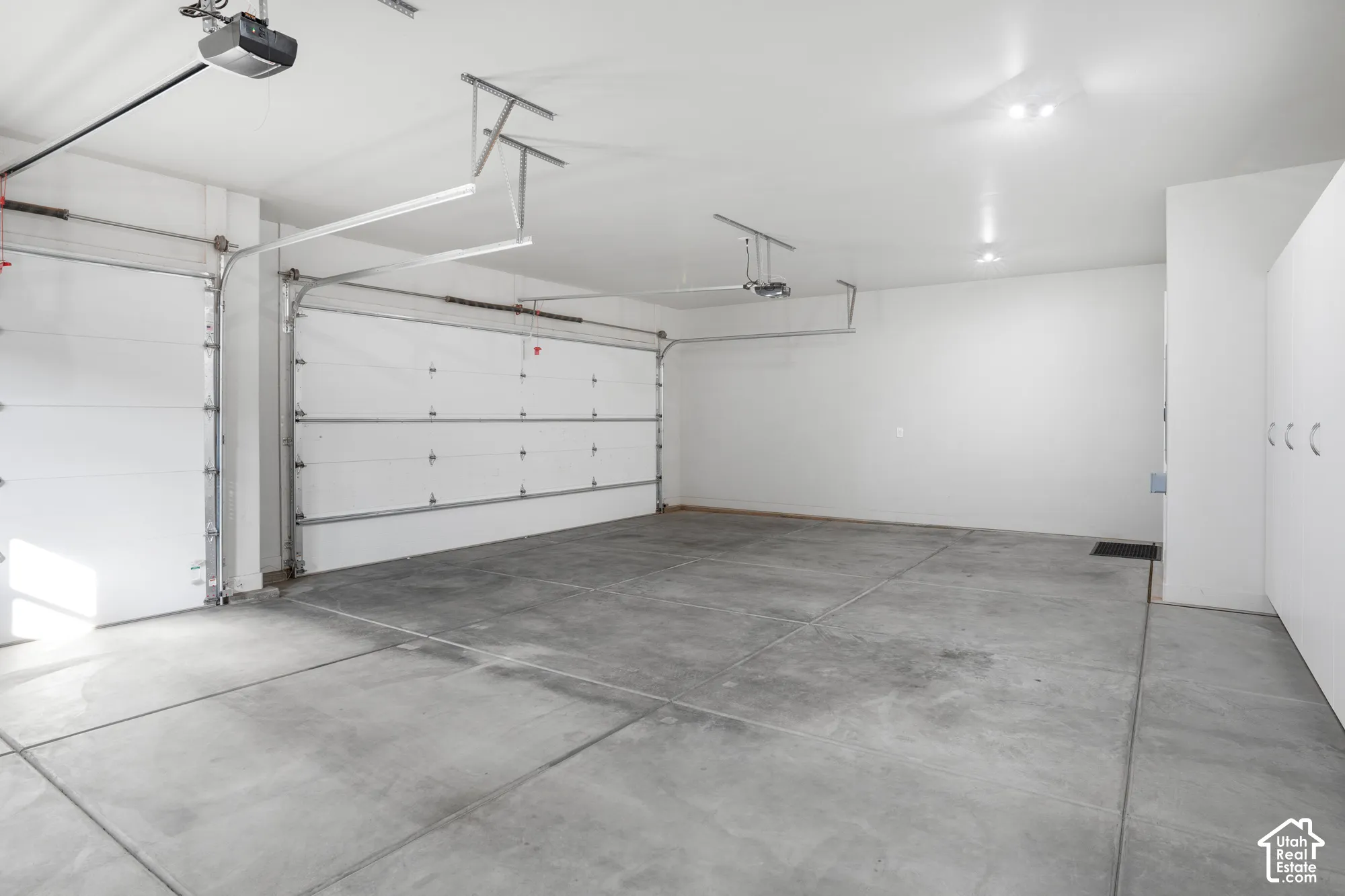 Two panel garage doors, concrete flooring, overhead lighting, and built-in white cabinetry