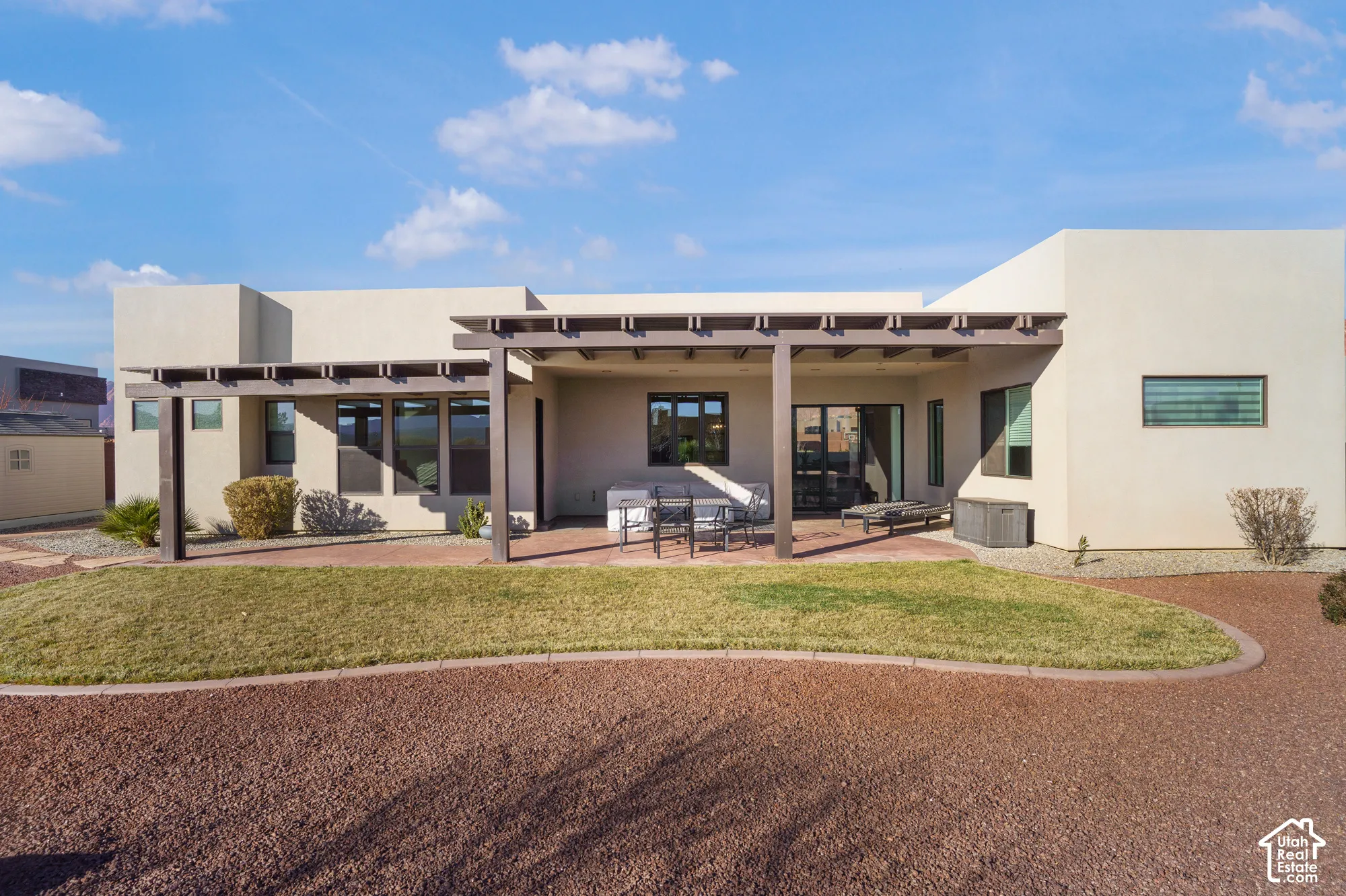 Stucco exterior with multiple windows, covered patio, pergola, and a manicured lawn