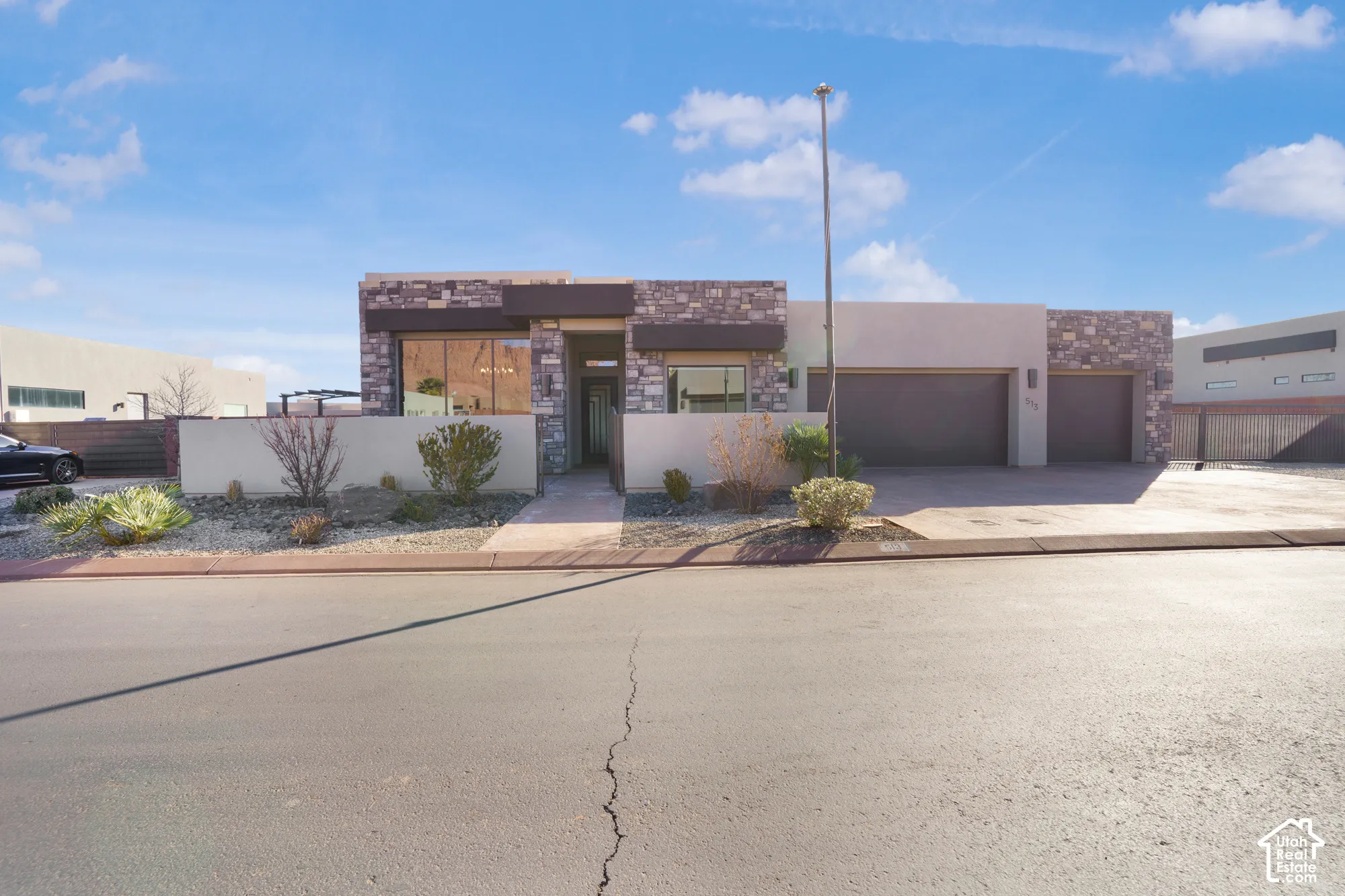 Contemporary stucco and stone exterior with large windows, an integrated two-car garage, and a concrete driveway