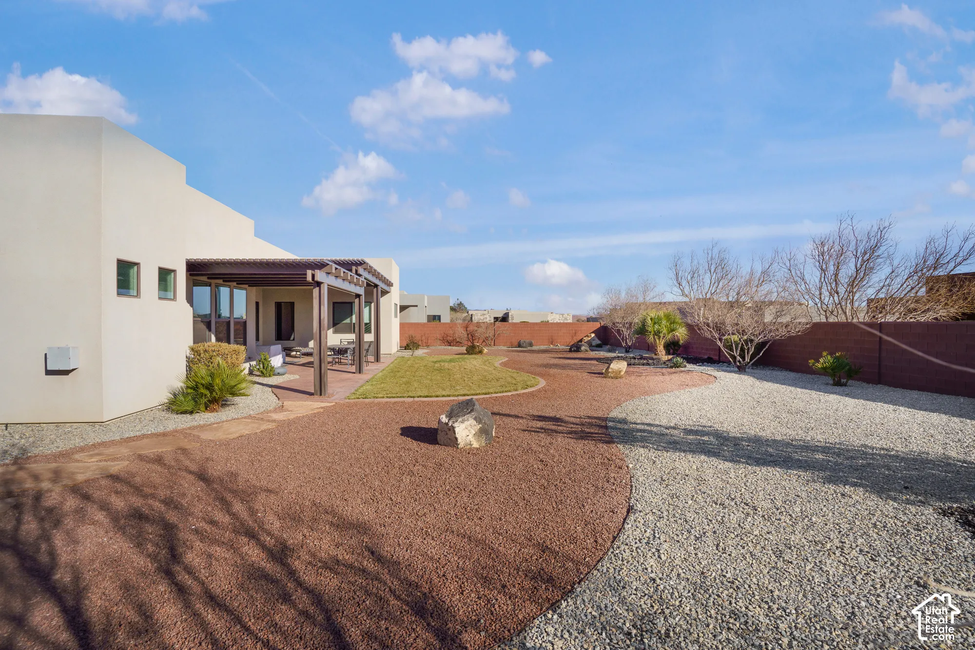 Expansive backyard featuring a covered patio with pergola, stucco exterior, mixed gravel landscaping, and a manicured lawn area