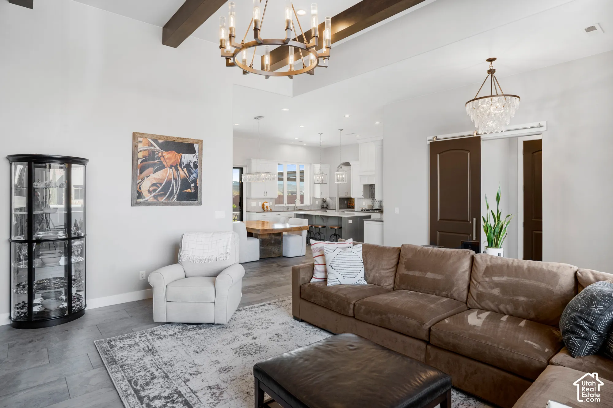 Spacious living area featuring exposed ceiling beams, a large chandelier, and gray wood-finish flooring