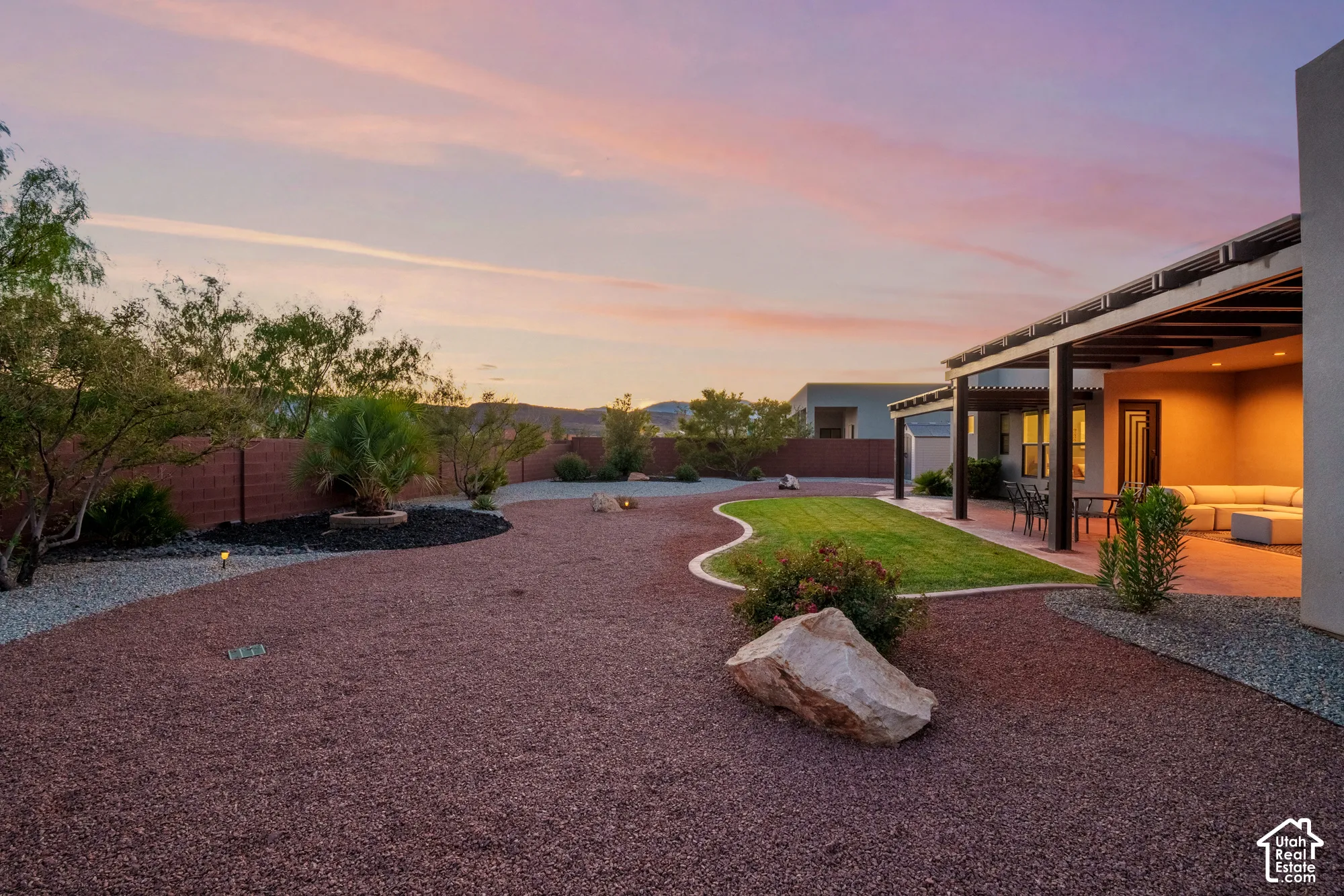 Expansive backyard featuring a covered patio, manicured lawn, gravel landscaping, and established plantings