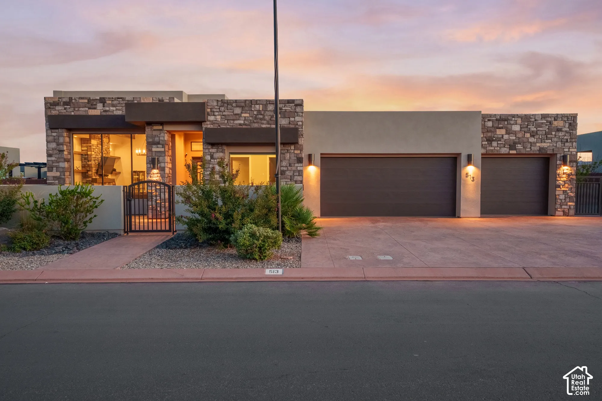 Stone and stucco exterior with multiple garage bays, an arched entryway gate, and integrated exterior lighting