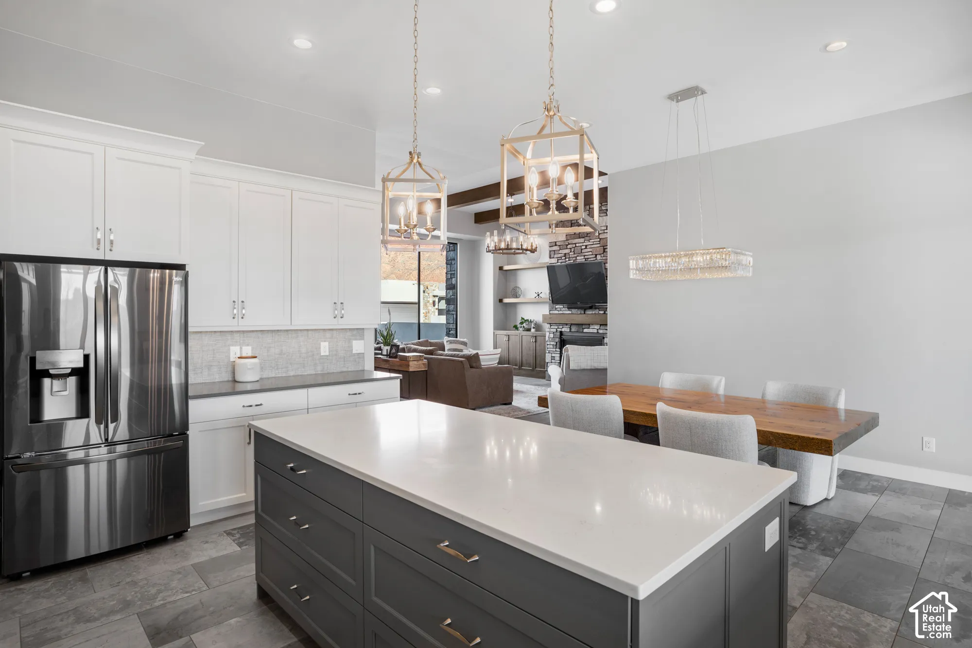 Spacious kitchen featuring an expansive island with a light-toned countertop, white upper cabinetry, and a stainless steel refrigerator