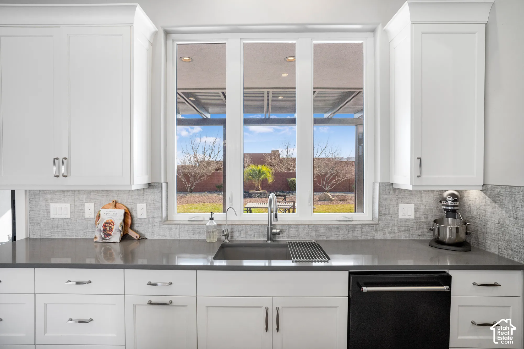 White shaker-style cabinetry, a deep basin sink, a large window, under-cabinet lighting, and a textured tile backsplash