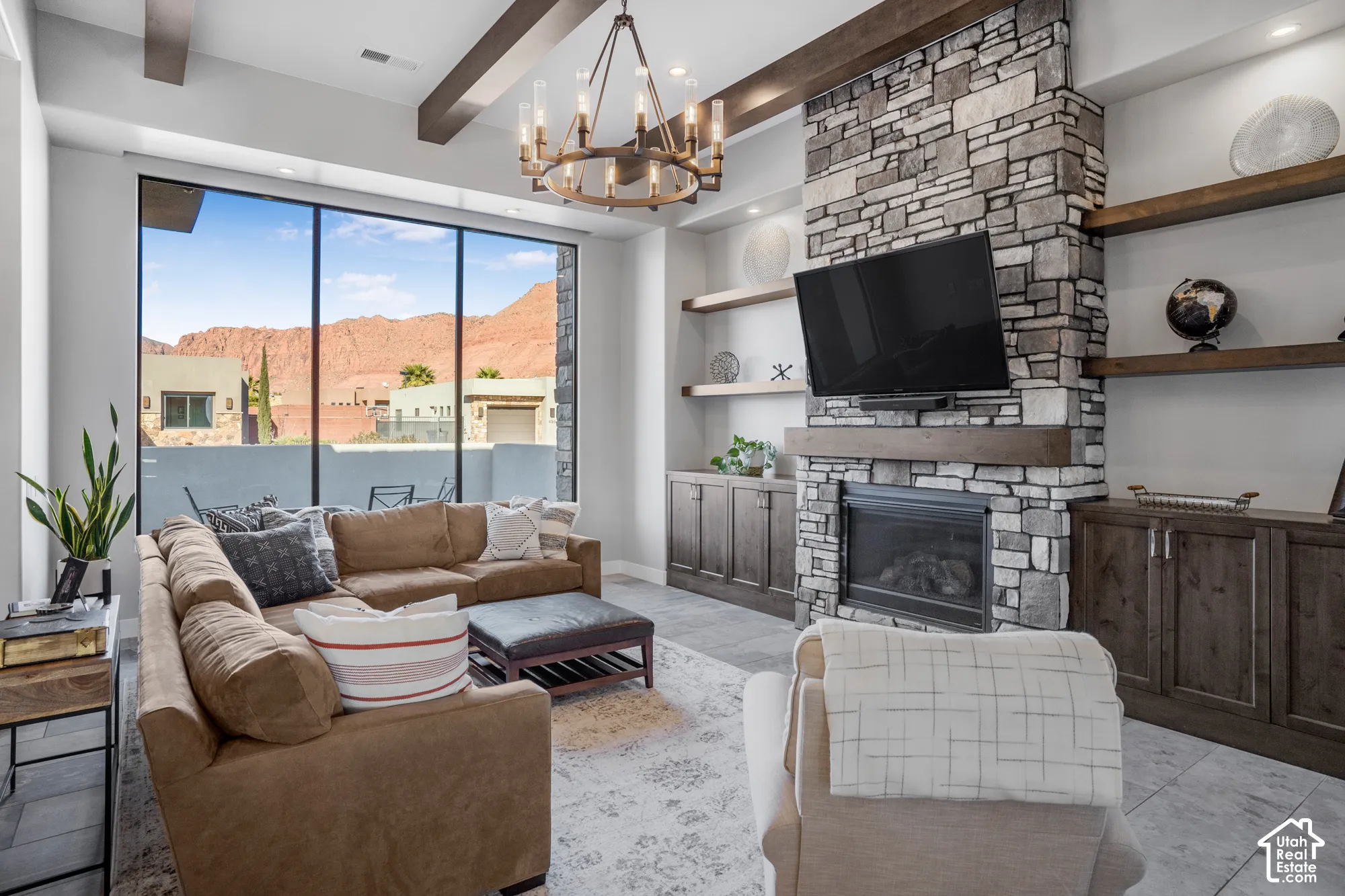 Expansive floor-to-ceiling windows, stone-clad fireplace, built-in shelving, custom cabinetry, and a decorative chandelier