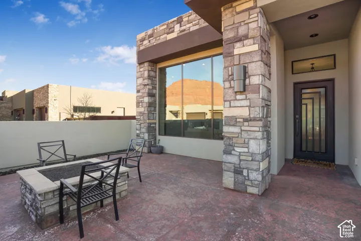 Exterior patio with a stone-clad fire pit, stamped concrete flooring, full-lite entry door, and large window