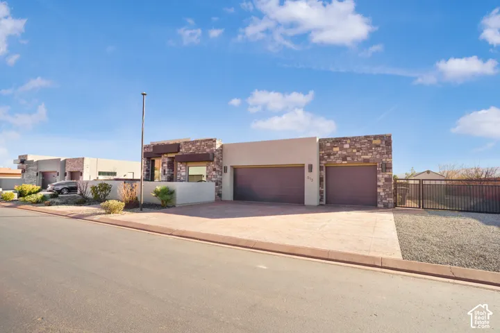 Modern exterior with stone and stucco facade, stamped concrete driveway, two-car garage, and secure gated side yard