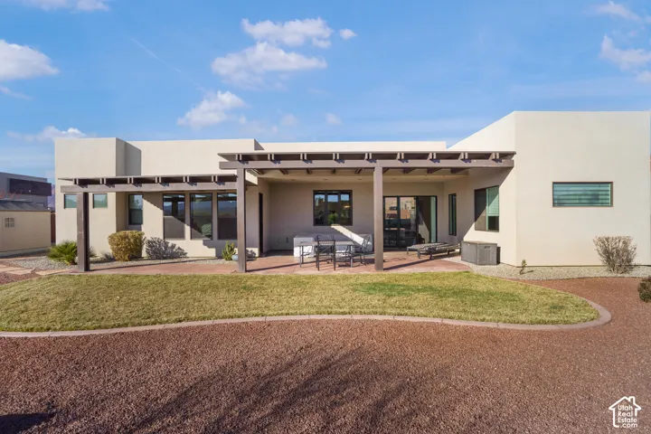 Stucco exterior with multiple windows, covered patio, pergola, and a manicured lawn