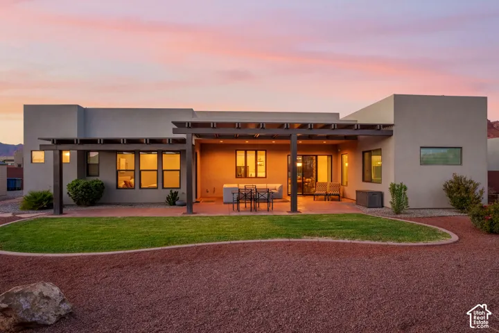 Expansive rear exterior with a covered patio, integrated pergola, and a manicured lawn