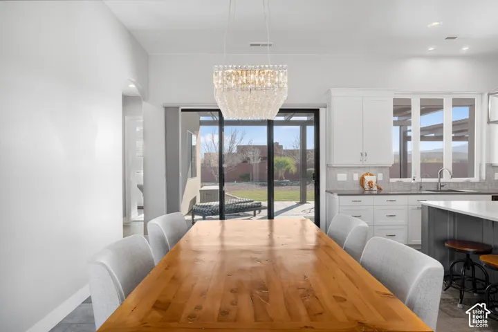 Open-concept dining area with a crystal chandelier, wood-finish flooring, and direct access to the outdoor patio through sliding glass doors