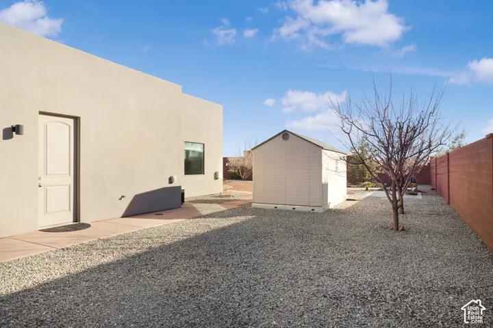 Exterior stucco finish, detached storage shed, gravel landscaping, side entrance, and permanent fencing