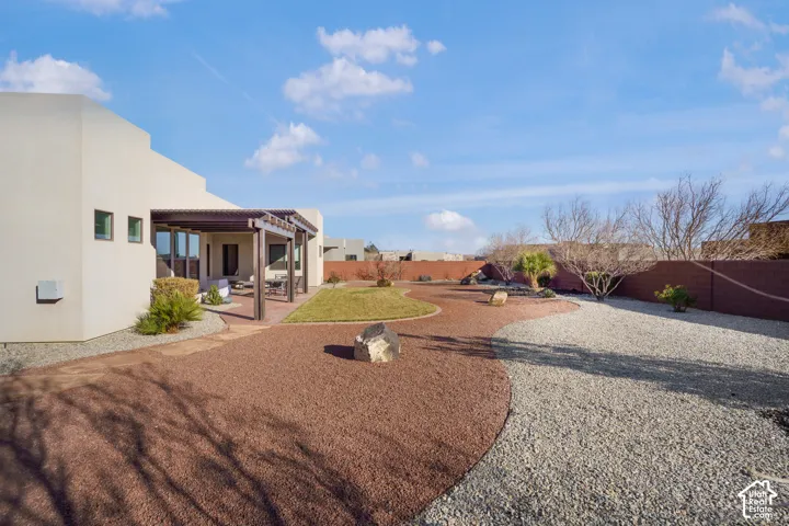 Expansive backyard featuring a covered patio with pergola, stucco exterior, mixed gravel landscaping, and a manicured lawn area