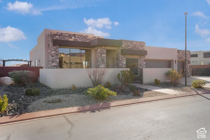 Contemporary exterior with stone accents and stucco siding, featuring a large picture window, an attached garage, and xeriscaping