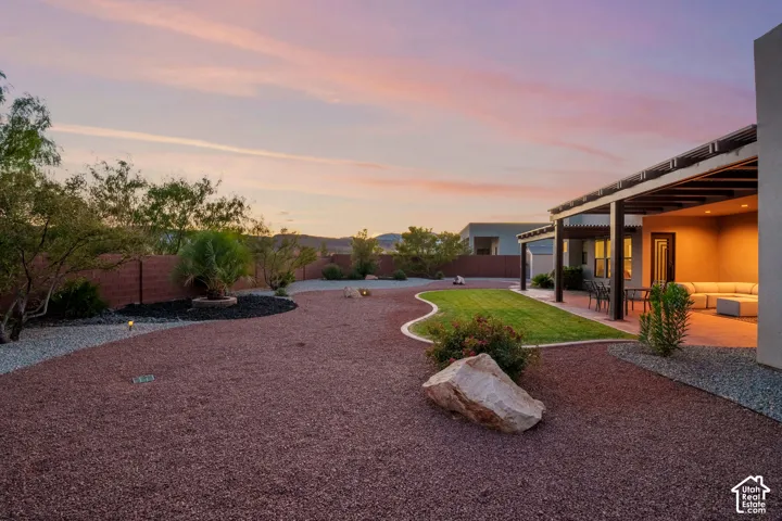 Expansive backyard featuring a covered patio, manicured lawn, gravel landscaping, and established plantings