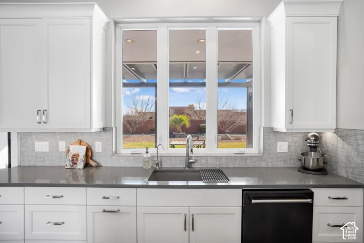White shaker-style cabinetry, a deep basin sink, a large window, under-cabinet lighting, and a textured tile backsplash
