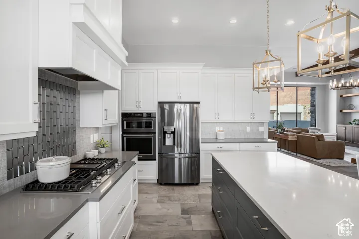 Gourmet kitchen with stainless steel appliances, white shaker cabinetry, an expansive island with a light-toned countertop, and a gas range with a decorative tile backsplash