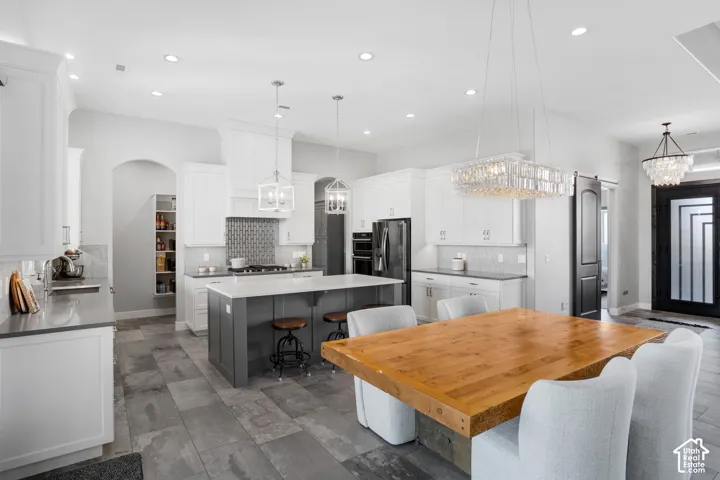 Open-concept kitchen and dining area featuring a two-tone kitchen island, white cabinetry, integrated stainless steel appliances, and tile flooring
