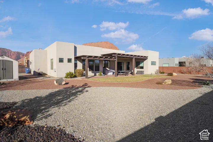Expansive exterior featuring a pergola-covered patio, landscaped yard with gravel and planted areas, and a detached storage shed