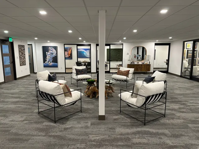 Recessed lighting throughout, gray patterned carpet, multiple glass-paneled doors, and a central structural column. Pictures from the previous tenant. The office is now vacant