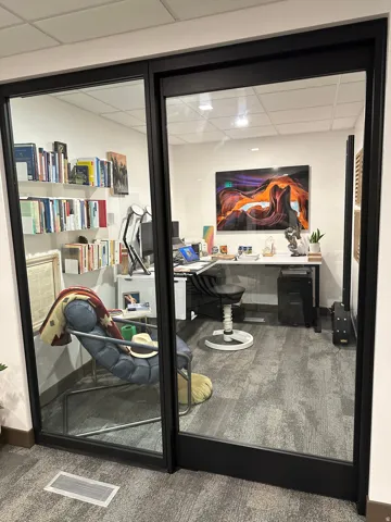 Room with glass wall and door featuring  white walls, and gray patterned carpet. Pictures from the previous tenant. The office is now vacant