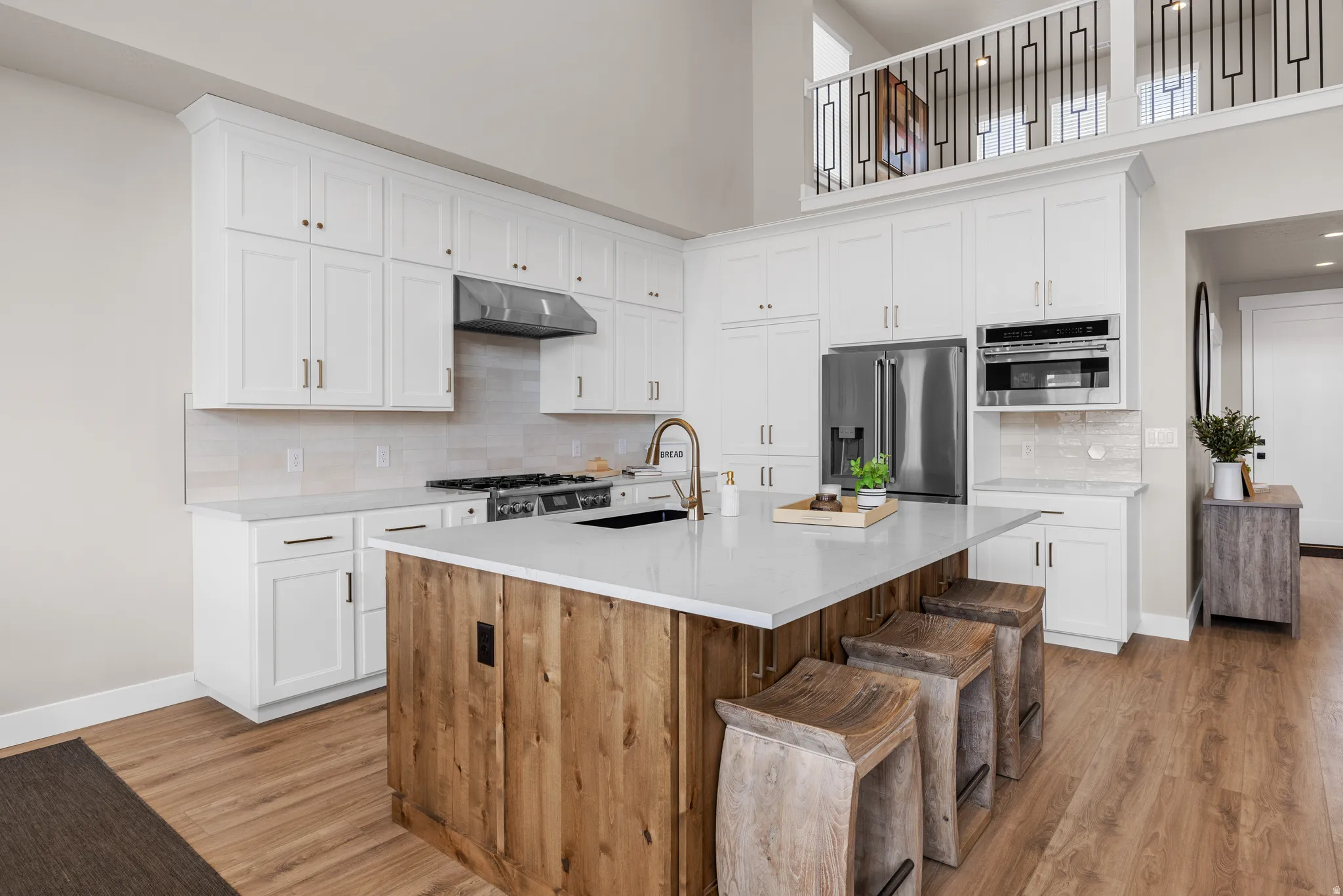 Kitchen featuring white cabinetry, wood-finish flooring, stainless steel appliances, a center island with a light-colored countertop, and a lofted space above