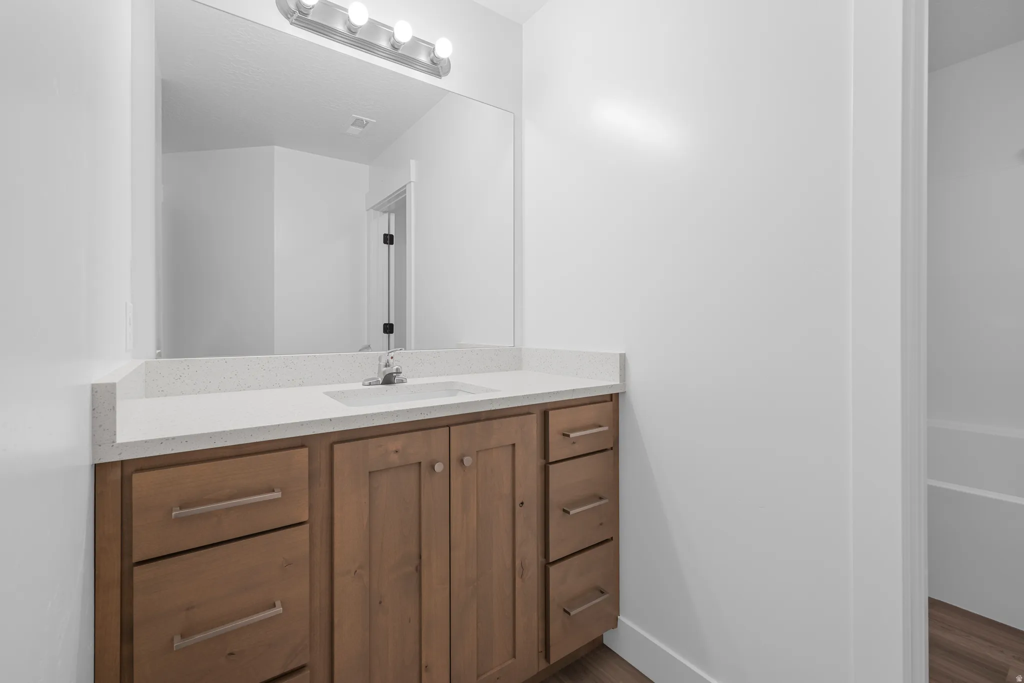 Bathroom vanity with light wood-finish cabinetry, white countertop, integrated sink, and large mirror with overhead lighting