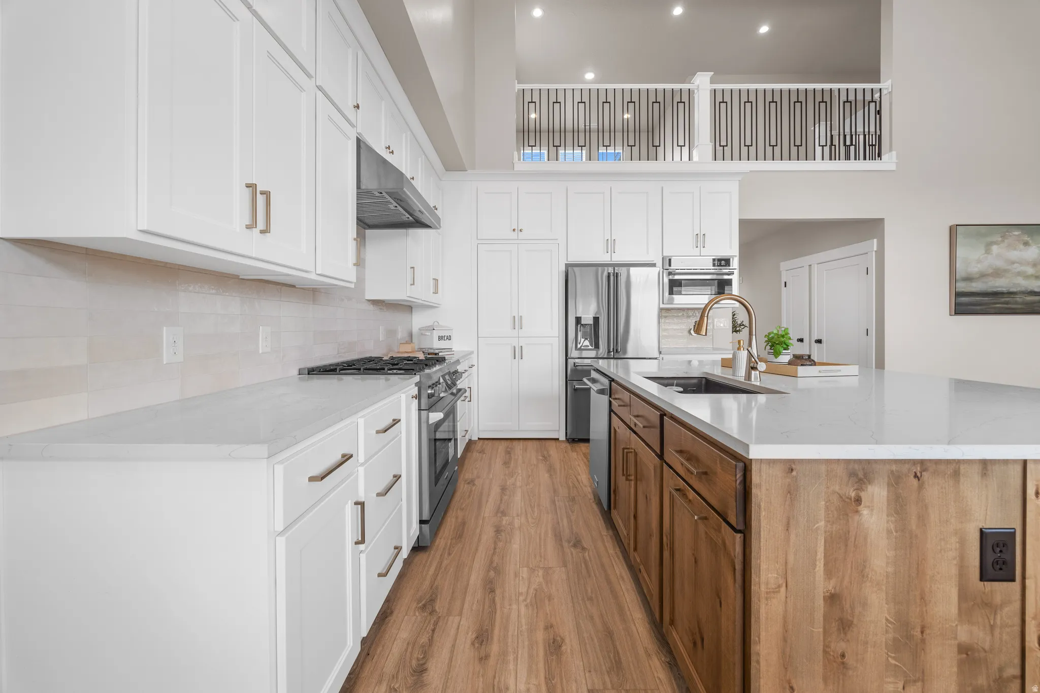 Gourmet kitchen featuring white cabinetry, light-toned countertops, a gas range, a central island with wood paneling, and wood-finish flooring