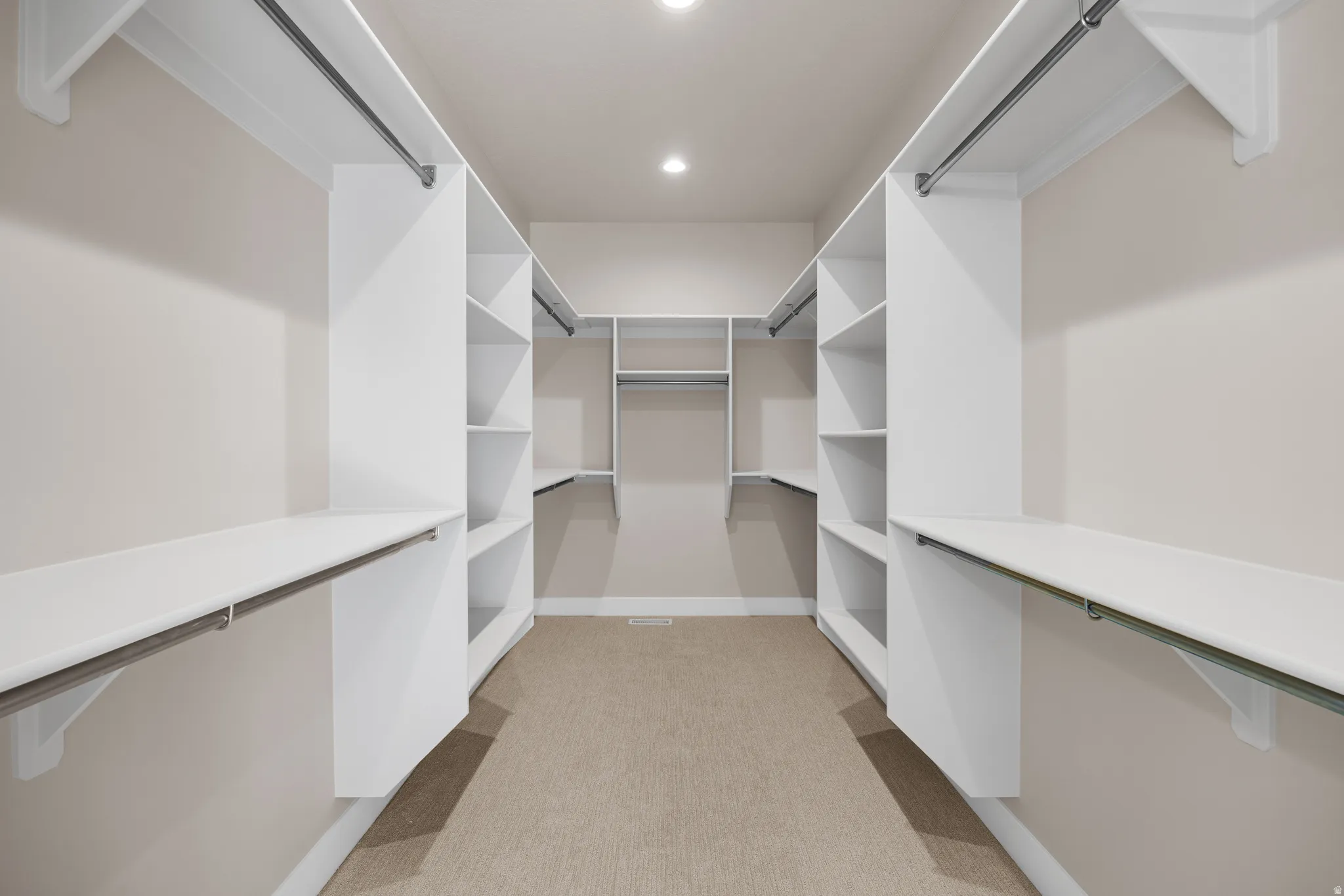 Expansive walk-in closet featuring white built-in shelving, multiple hanging rods, recessed lighting, and soft carpet flooring