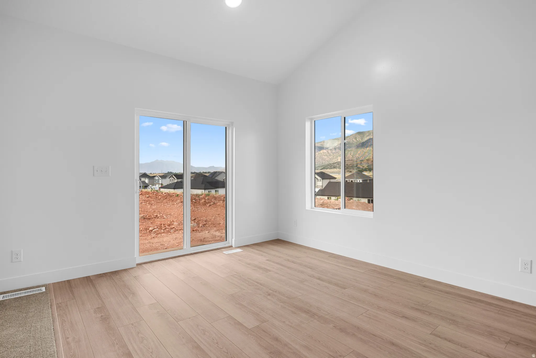 Vaulted ceiling, wood-finish flooring, white walls, sliding glass door, and a single pane window
