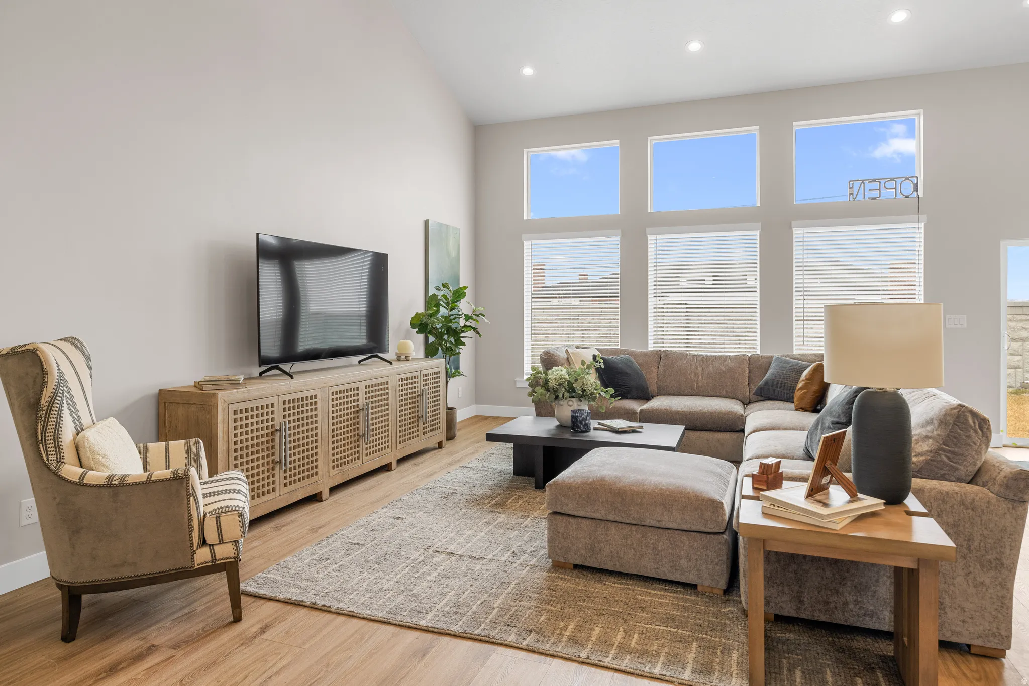 Vaulted ceiling, wood-finish flooring, recessed lighting, large windows with blinds, and a built-in media console