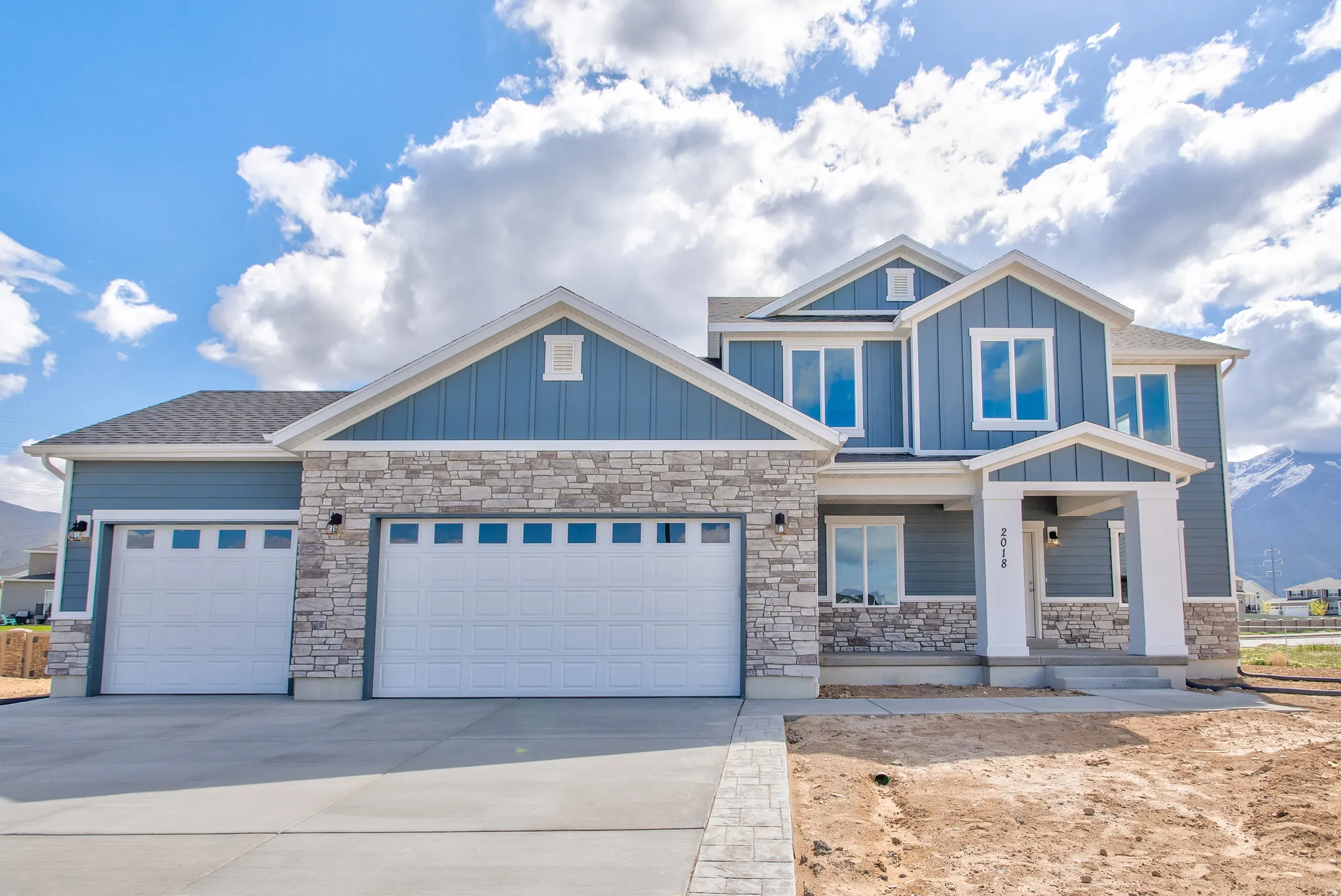 Two-story residence featuring blue siding with stone veneer accents, a three-car garage, and a covered entry porch
