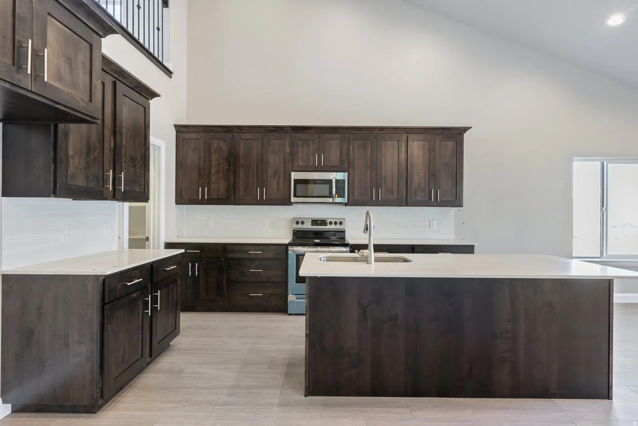 Kitchen featuring dark wood cabinetry, light countertops, stainless steel appliances, a center island with a sink, and a vaulted ceiling