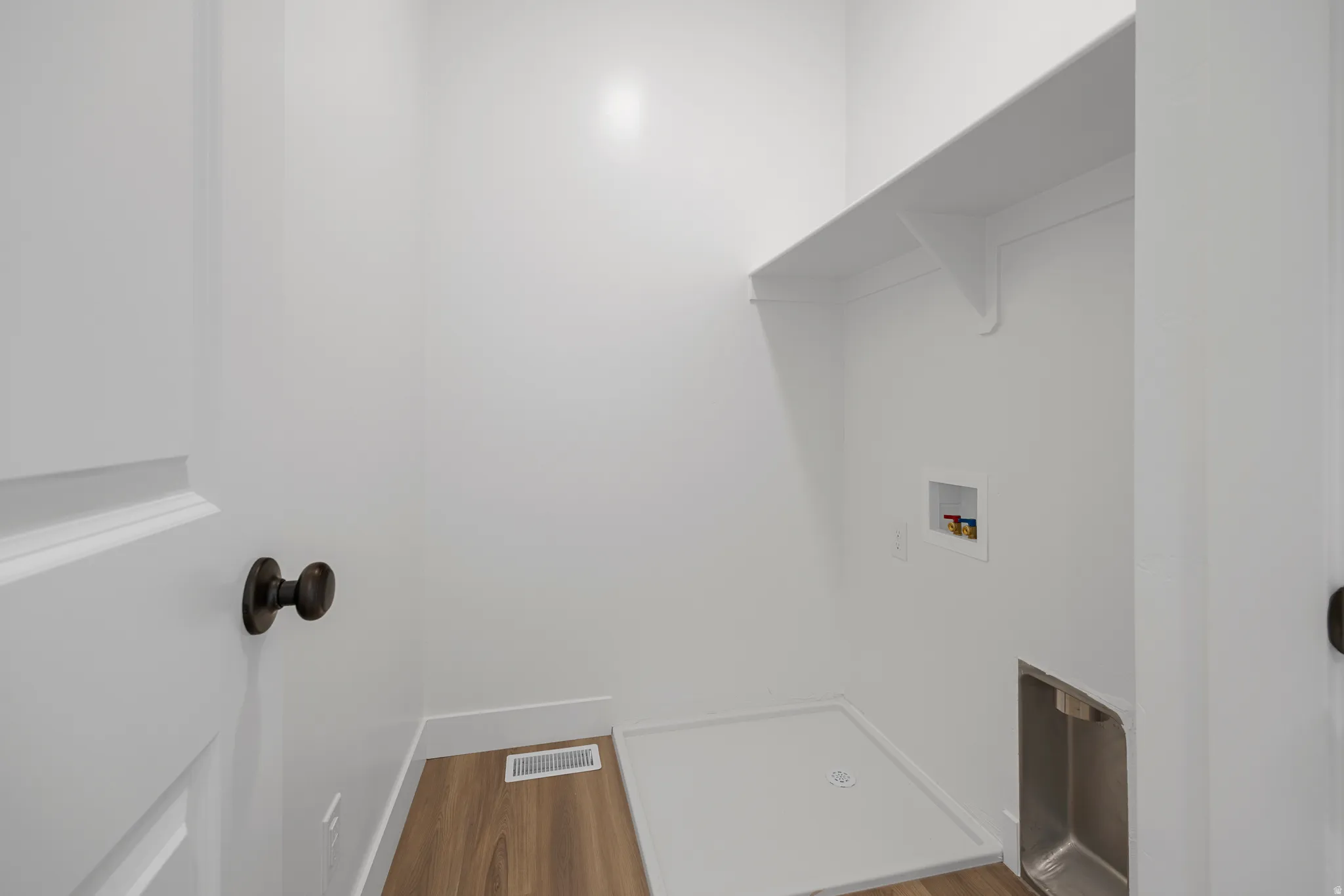 Utility room with wood-finish flooring, built-in shelving, and a stainless steel utility sink