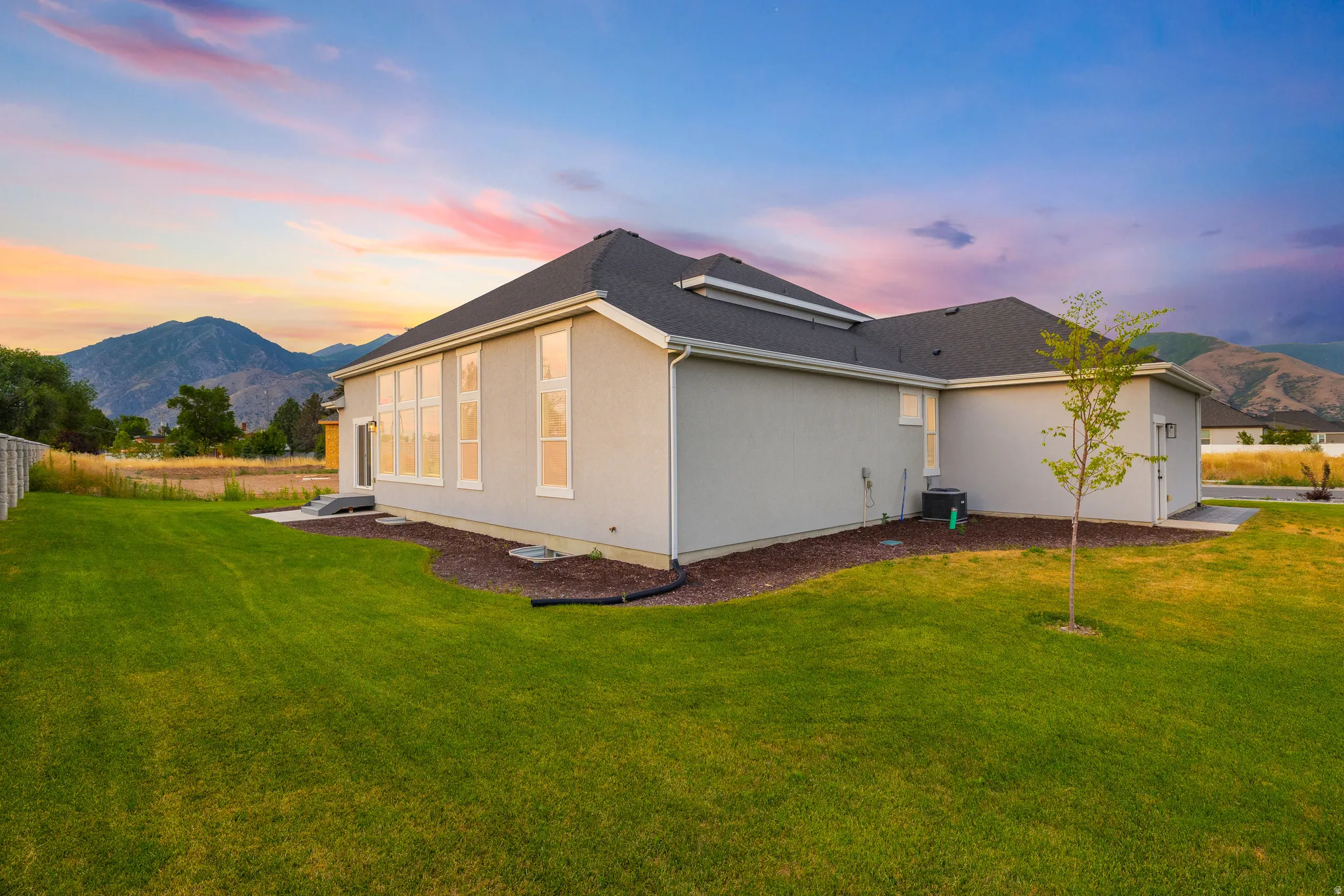 Expansive backyard featuring a manicured lawn, stucco exterior, multiple large windows, and a mountain backdrop