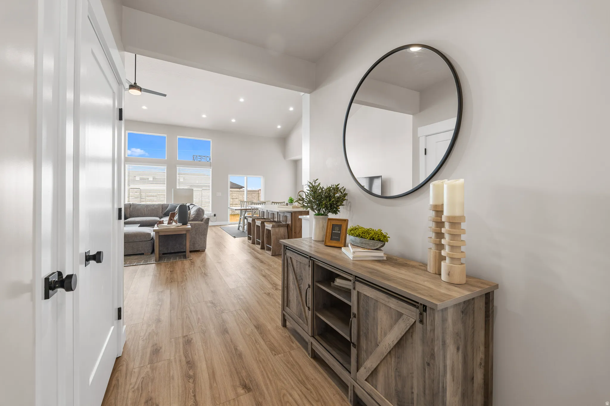 Light-toned wood-finish flooring extending into the living area, vaulted ceilings with recessed lighting, and a large window arrangement providing natural light