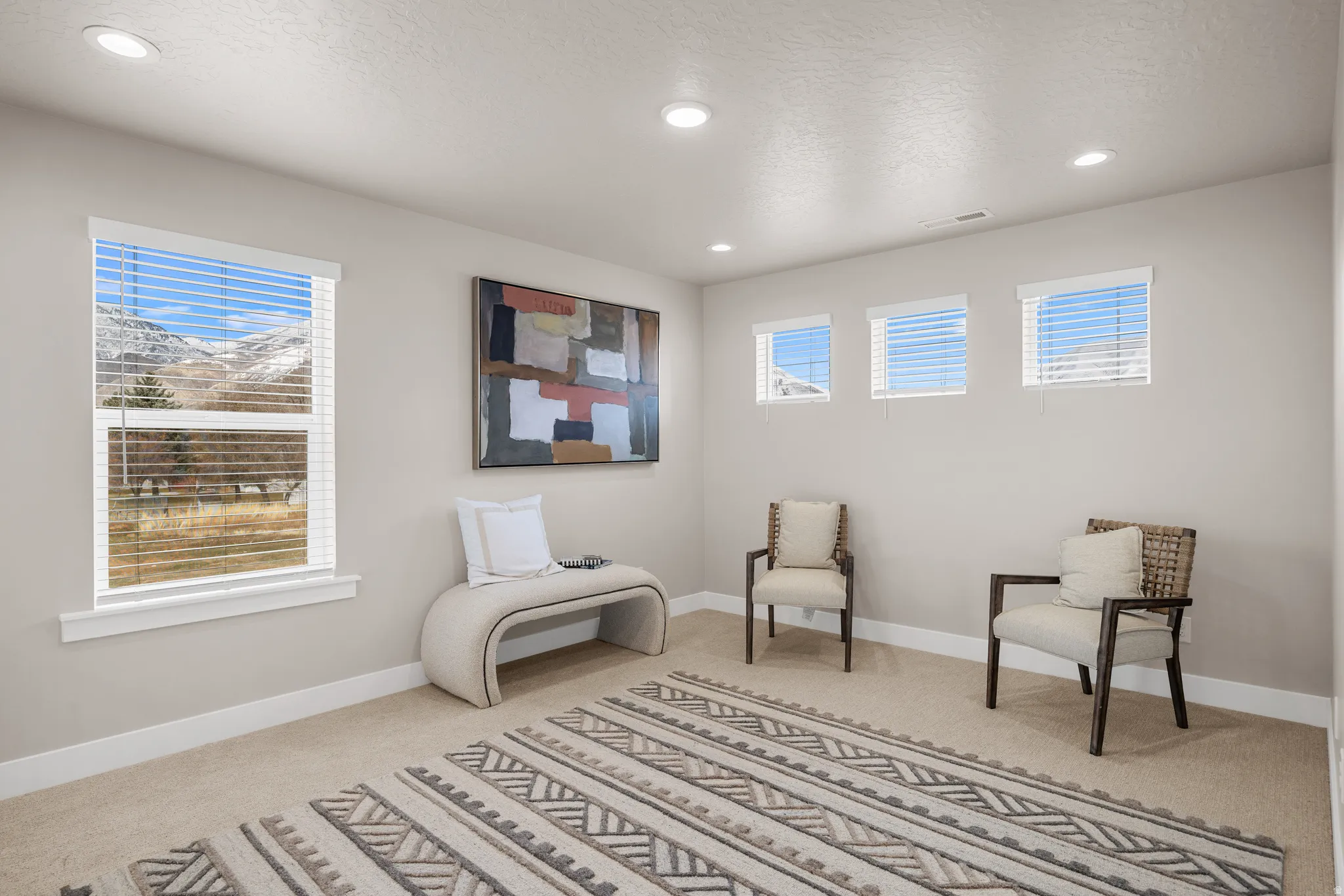 Recessed lighting, large window, three smaller windows, neutral wall tones, and carpeted flooring