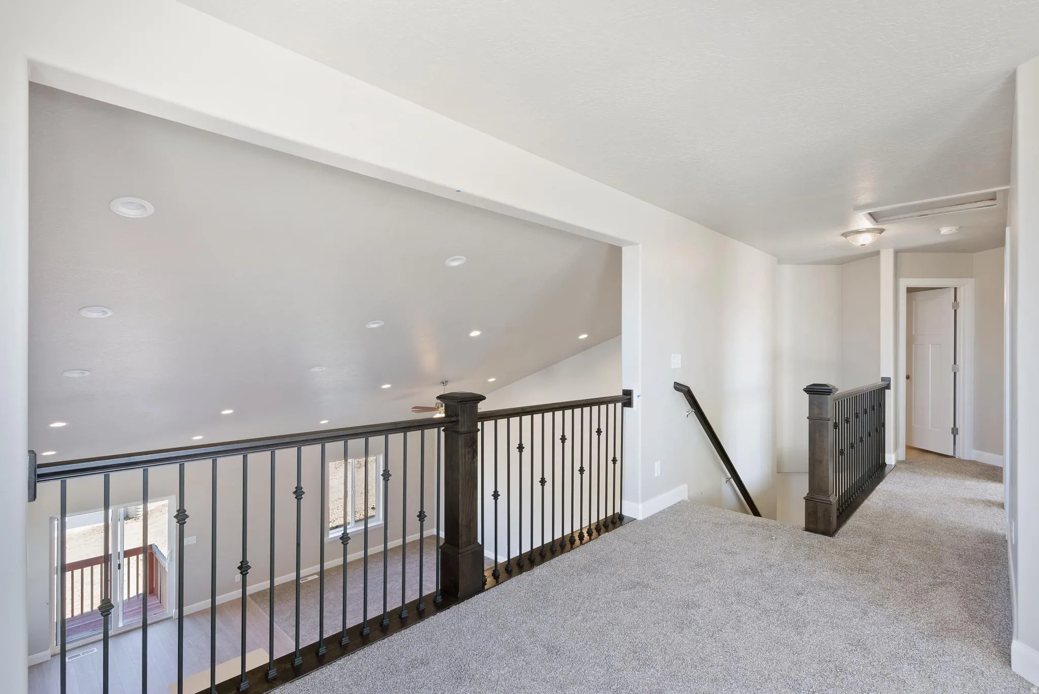 Carpeted hallway with wrought iron railing, recessed lighting, and a white paneled door