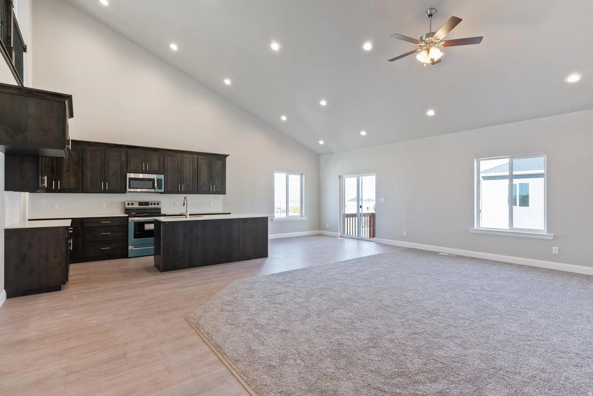 Vaulted ceiling with recessed lighting, dark wood cabinetry, white countertops, stainless steel appliances, and a sliding glass door to exterior