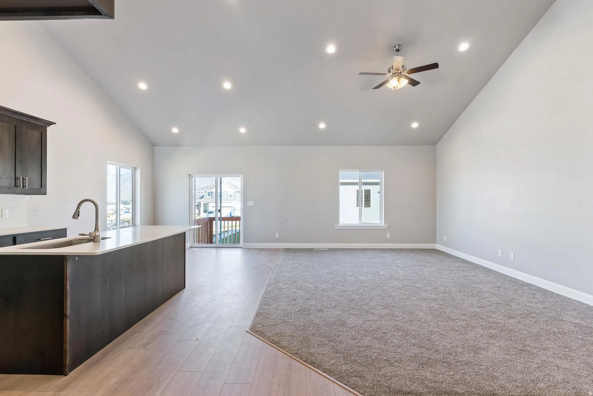 Vaulted ceiling with recessed lighting and a ceiling fan, kitchen island with an undermount sink and gooseneck faucet, wood-finish flooring, and sliding glass doors to the exterior
