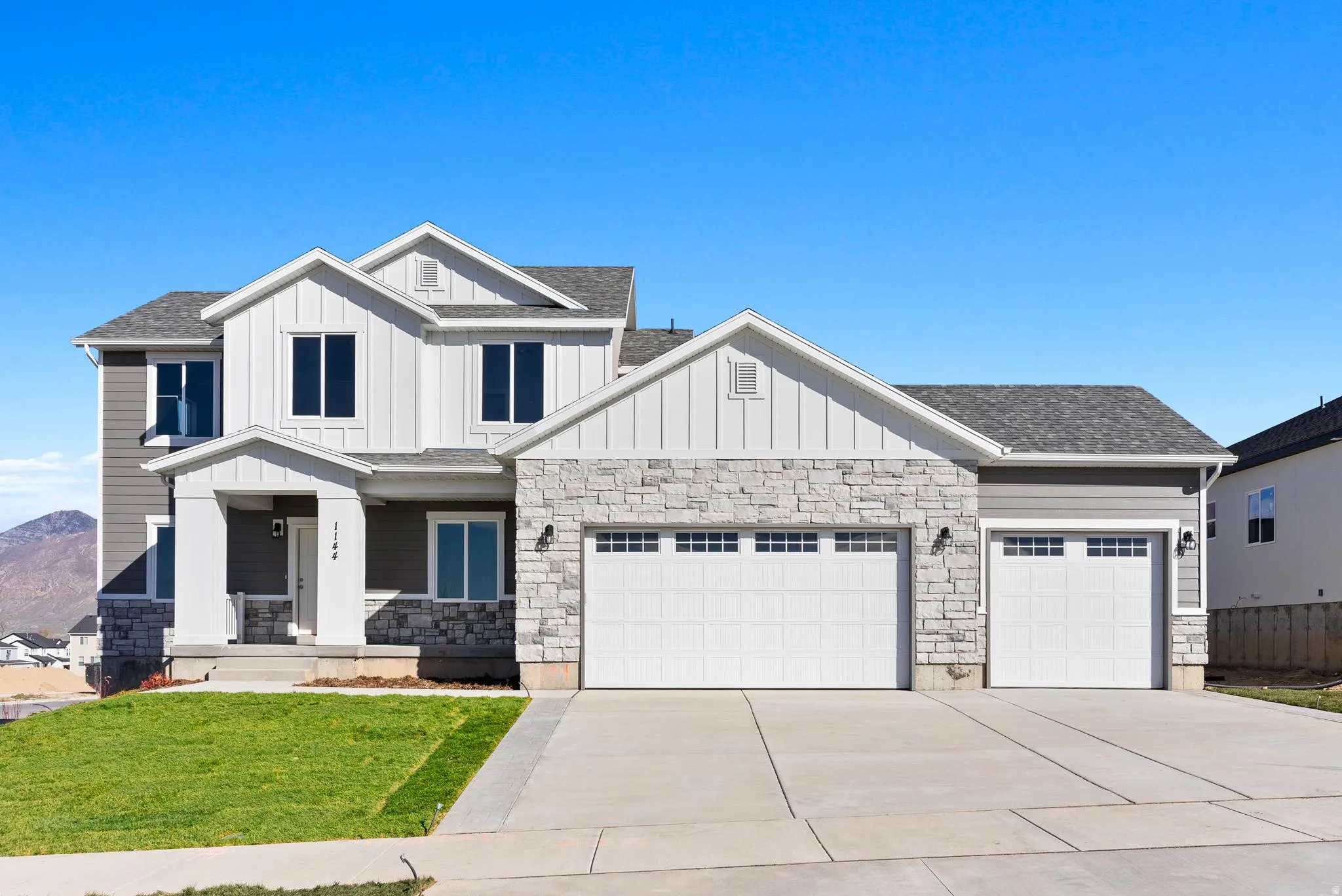 Contemporary two-story residence with a gray and white exterior featuring stone accents and board-and-batten siding
