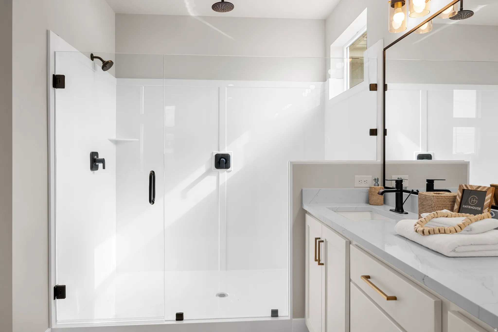 Walk-in shower with clear glass enclosure and matte black fixtures, rain showerhead, vanity with undermount sink and stone countertop, and gold-toned hardware