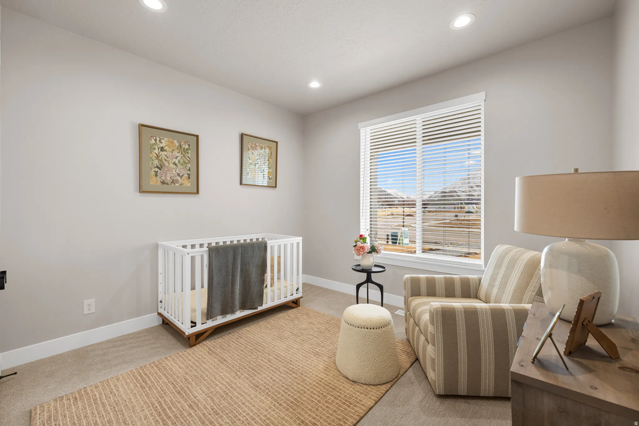 Recessed lighting illuminates a carpeted room featuring a large window with blinds and neutral-toned walls