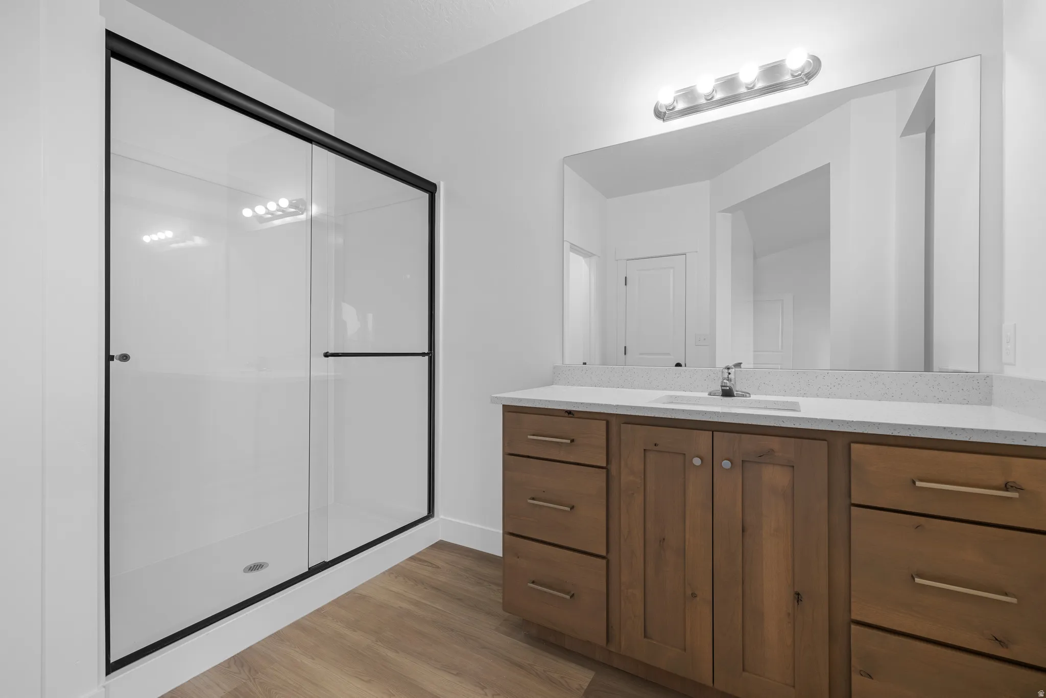 Bathroom featuring a wood-finish vanity with a light-colored countertop, an undermount sink, and a framed mirror with overhead lighting