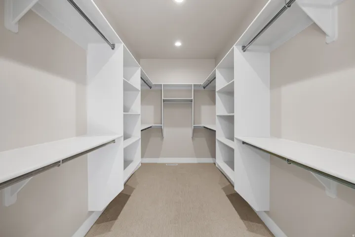 Expansive walk-in closet featuring white built-in shelving, multiple hanging rods, recessed lighting, and soft carpet flooring