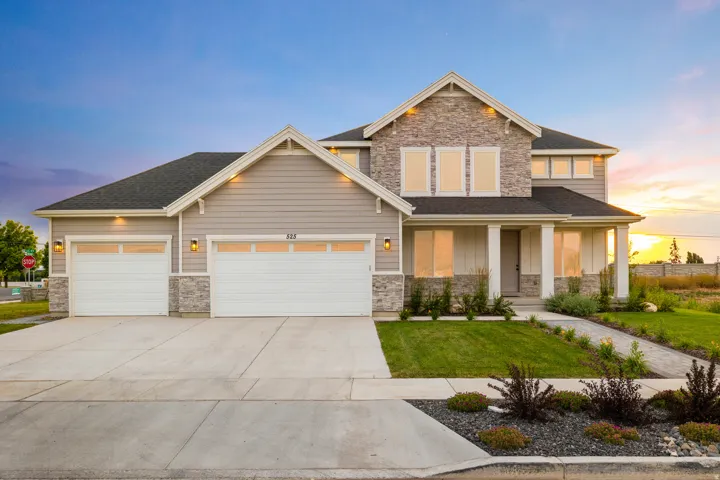 Two-story residence featuring a stone and siding exterior, a two-car garage, a covered entry with columns, and a landscaped front yard with a concrete driveway