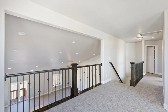 Carpeted hallway with wrought iron railing, recessed lighting, and a white paneled door